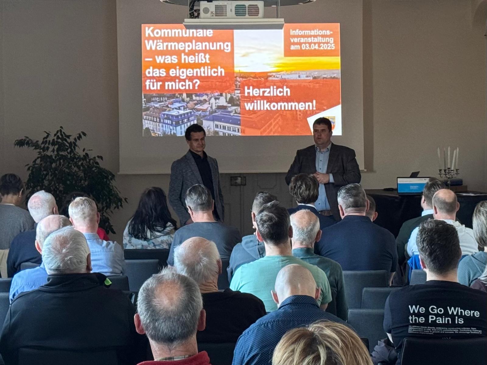 Das Foto wurde während der Veranstaltung aufgenommen. Es zeigt Oberbürgermeister Frank Höhme und Energiemanager Matthias Herfter vor den Gästen der Veranstaltung.